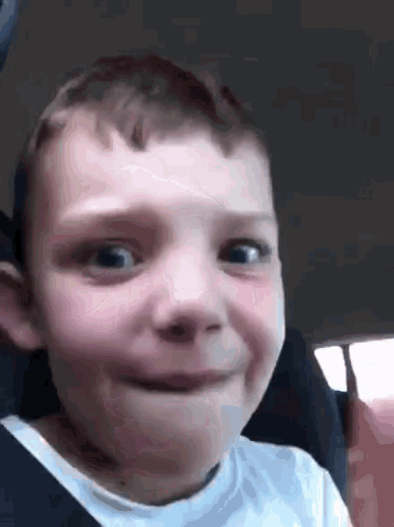 a young boy in a car seat is making a funny face .