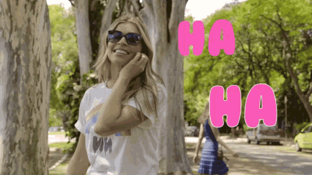 a woman wearing sunglasses stands in front of a sign that says " ha ha "