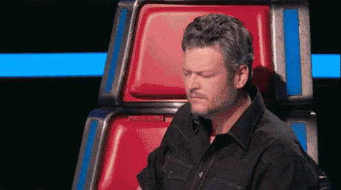 a man in a black shirt is sitting in a red chair and making a face .