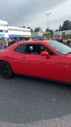 a red car is parked in a parking lot with a crowd of people watching .