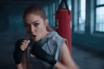 a woman is wearing boxing gloves and kicking a punching bag in a gym .