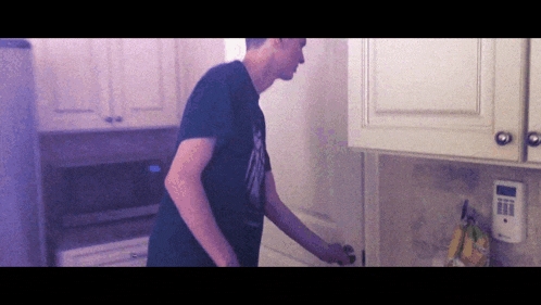 a man in a black shirt is standing in a kitchen near a clock