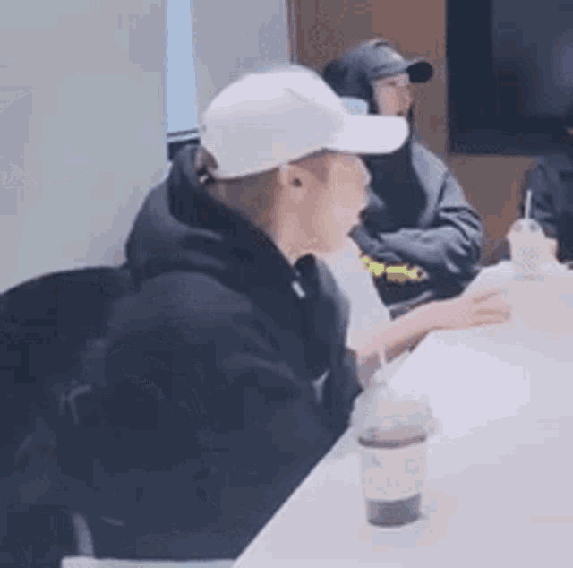 a man wearing a white baseball cap is sitting at a table with a cup of coffee .