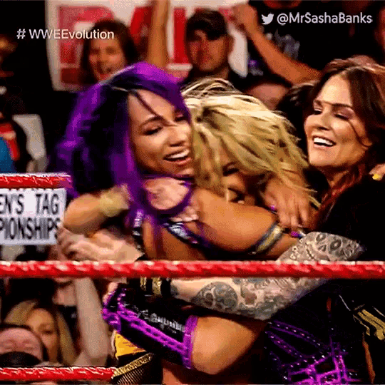 three women hugging in a wrestling ring with a sign that says ' en 's tag championships '