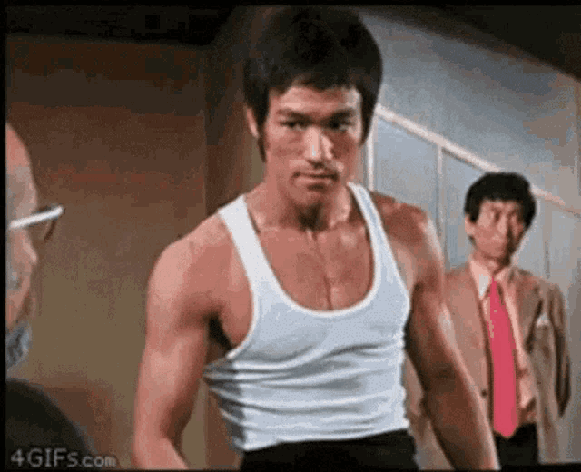 bruce lee is wearing a white tank top and a red tie while standing in front of two men .