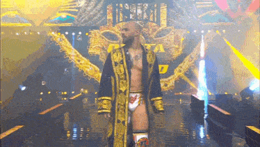 a wrestler in a gold robe is walking down a ring .
