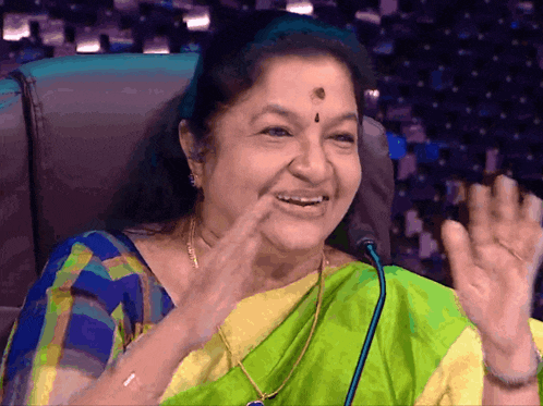 a woman in a green and yellow saree is smiling and talking into a microphone