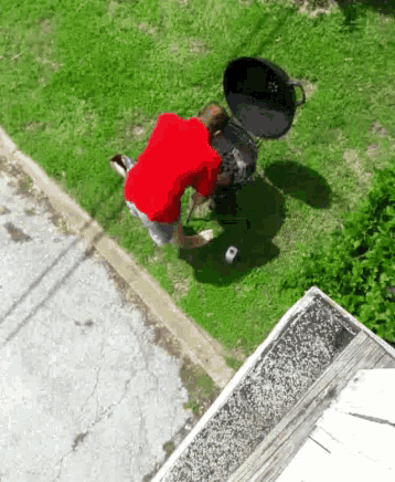 a man in a red shirt is kneeling next to a barbecue grill