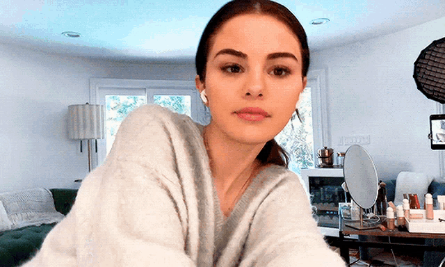 a woman in a grey sweater is looking at the camera in a living room