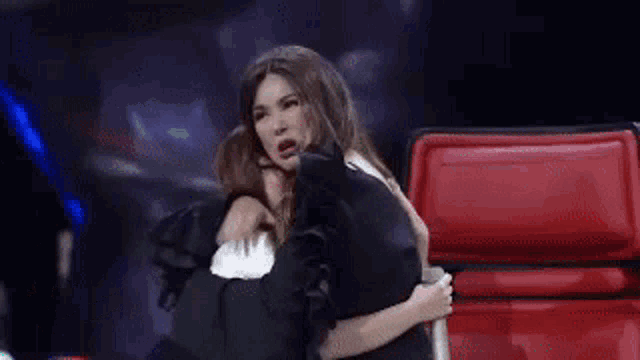 two women are hugging each other on a stage in front of a red chair .