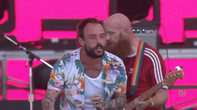 a man with a beard is singing into a microphone while another man plays a guitar on stage .