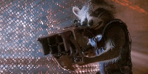 rocket raccoon from guardians of the galaxy is holding a machine gun .