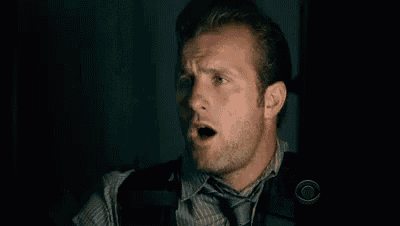 a man in a shirt and tie is making a surprised face in a dark room .