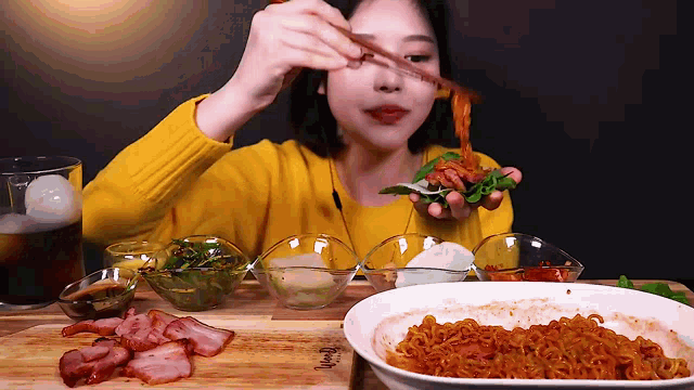 a woman in a yellow sweater is eating a sandwich with chopsticks