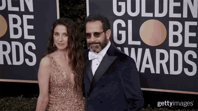 a man and woman are posing for a picture in front of a golden globe sign