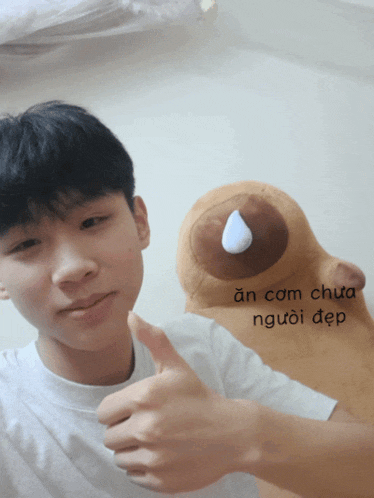 a young man giving a thumbs up next to a stuffed animal that says an cam chua người đẹp