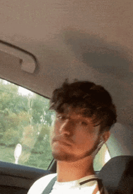 a man with a beard is sitting in the back seat of a car looking at the camera