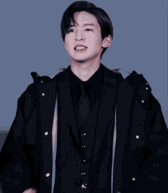 a young man wearing a black jacket and tie is making a face
