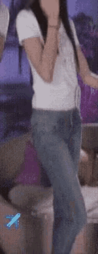a woman in a white shirt and blue jeans is dancing in front of a blue airplane