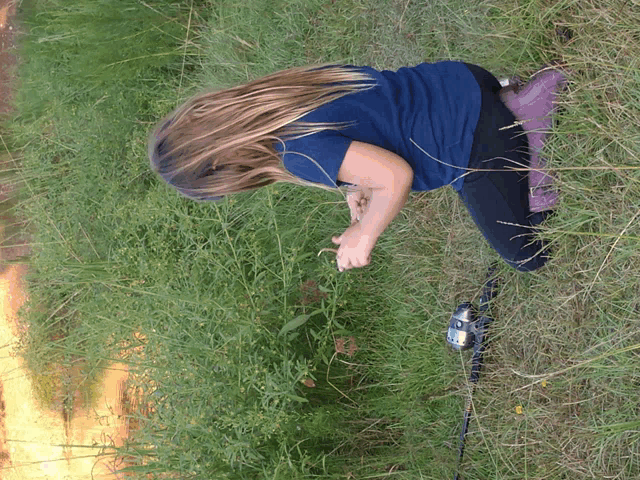 a girl in a blue shirt kneeling in the grass