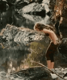 a woman in a bikini is standing on a rock near a river .