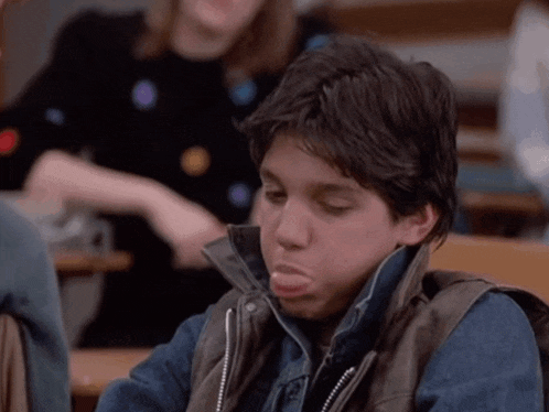 a young boy making a funny face while wearing a leather vest
