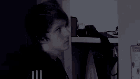 a young man is standing in a closet with clothes hanging on the shelves .