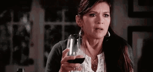 a woman is holding a glass of red wine and making a funny face .