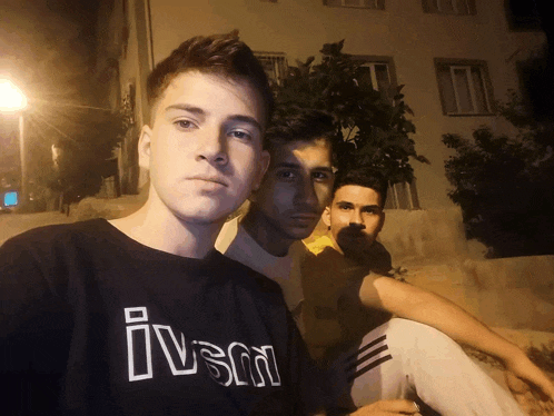three young men are posing for a picture and one of them is wearing a black shirt that says ivsm