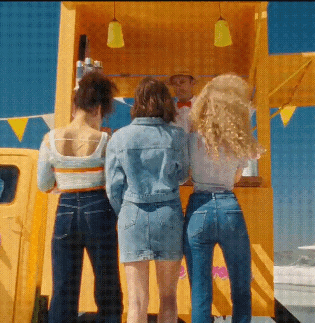 three women are standing in front of a yellow van