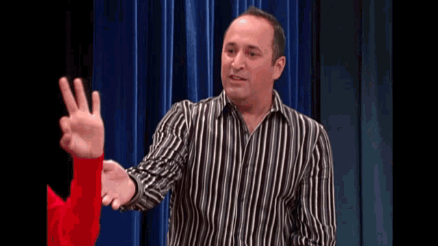 a man in a black and white striped shirt holds up his fingers