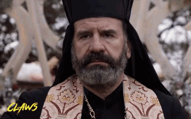 a man with a beard is wearing a priest 's robe and a hat with the word claws on the bottom