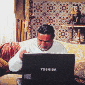 a man sits on a couch looking at a toshiba laptop