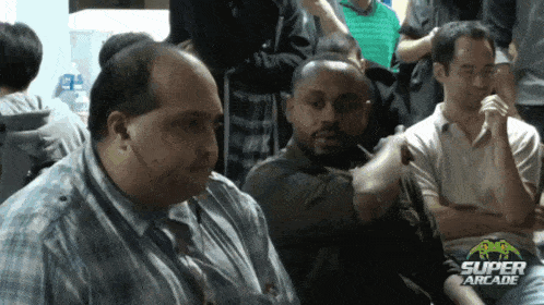 a group of men are sitting in a room with a super arcade logo on the bottom