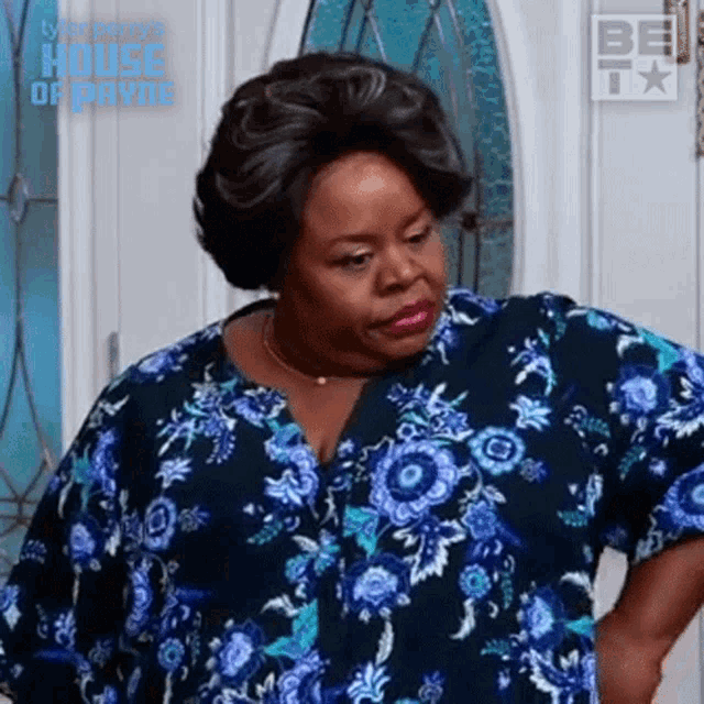 a woman in a blue floral shirt is standing in front of a door with the words house of payne on it