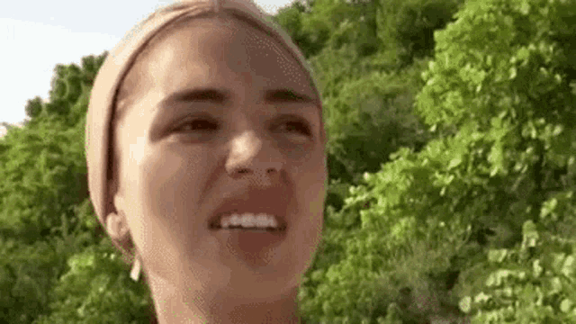 a close up of a woman 's face with trees in the background and trees in the background .