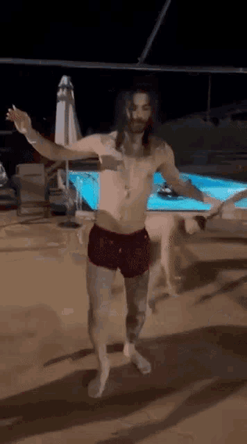 a shirtless man is dancing in front of a pool at night