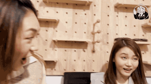 two women are laughing in front of a wall with shelves