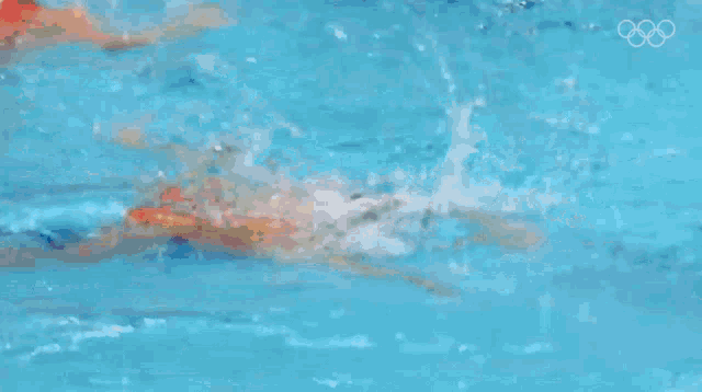 a woman is swimming in a pool with the olympic rings visible in the background