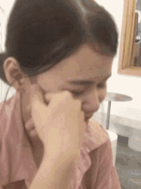 a woman in a pink shirt is covering her face with her hand .