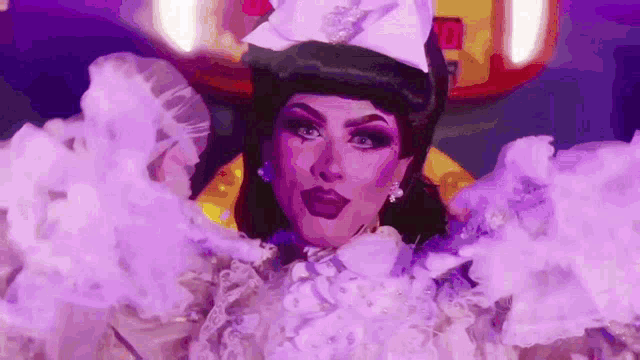 a drag queen is wearing a white hat and a purple dress and smoke is coming out of her mouth .