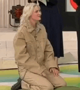 a woman in a khaki jacket is kneeling down on a green pillow .