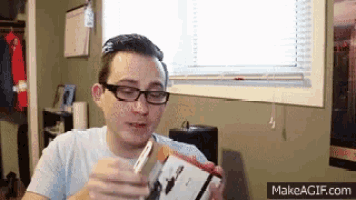 a man wearing glasses is holding a box that says makeagif.com on the bottom