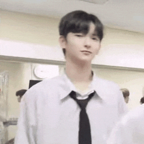 a young man wearing a white shirt and black tie is standing in front of a mirror .