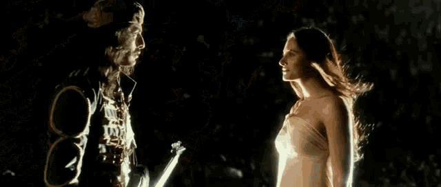 a man and a woman are standing next to each other in the dark . the woman is wearing a strapless dress .