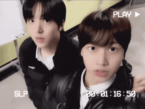 two young boys are standing next to each other and a play button is visible