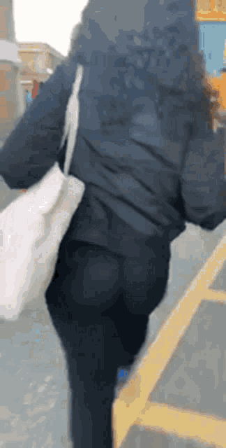 a woman in a black jacket and leggings is walking down a street .