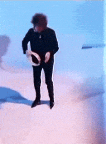 a man in a black suit is dancing with a tambourine in his hand