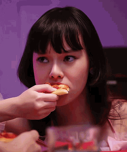 a woman eating a slice of pizza with a purple light behind her