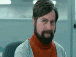 a man with a beard is sitting in a chair and making a face .